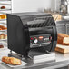 A black Hatco conveyor toaster machine on a counter with toasted bread on a metal rack.