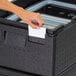 A hand placing a plastic ID label into a black plastic box on a table.