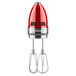 A KitchenAid candy apple red hand mixer with whisk attachment and stainless steel beaters.