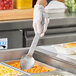 A person in gloves holding a Vollrath stainless spoon over food.