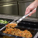 A person holding a Vollrath Jacob's Pride heavy-duty stainless spoon over a bowl of food.