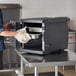 A person opening a black Cambro Cam GoBox food pan carrier to reveal a metal container inside.