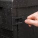 A hand opening a black Cambro Cam GoBox front loader latch.
