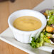 A plate of salad with a CAC Bone White China Ramekin of sauce on the side.