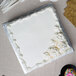 A white cake with frosting on a silver square cake drum with utensils.