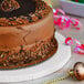 A white Enjay 10" round cake drum under a chocolate cake with chocolate shavings on top.