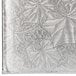 A close up of a silver Enjay cake board with a pattern of leaves and vines.