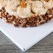 A white Enjay square cake drum with a frosted cake and nuts on top.