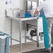 A man in a white shirt and blue apron cleaning dishes at a Regency clean dish table with a left drainboard.