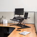 A black Luxor adjustable two-tier standing desk with a laptop and monitor on it.