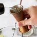 A hand using an American Metalcraft Antique Copper Japanese Style Jigger to pour liquid into a metal cup.