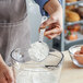 A person using a Vollrath stainless steel measuring spoon to measure flour into a bowl.