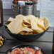 A black melamine serving bowl filled with chips on a table with a bowl of salsa.