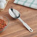 A silver Vollrath stainless steel measuring scoop on a wooden surface.