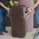 A man and woman standing next to a Continental brown square trash can with two doors.