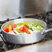 A Vollrath Wear-Ever saute pan filled with vegetables on a stove.