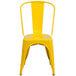 A yellow metal Flash Furniture outdoor restaurant chair with a vertical slat back and drain hole seat.