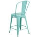 A green galvanized steel counter height stool with a vertical slat back and drain hole seat.