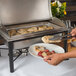 A person putting food on a plate from an Acopa wrought iron chafer.