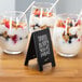 Three small glass bowls of yogurt with fruit and berries and a mini chalkboard tent sign that says breakfast, lunch, and dinner.