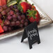 A tray of fresh fruit with American Metalcraft mini chalkboard tent signs on a table in a farm-to-table restaurant.