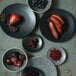 A table set with Luzerne Urban by Oneida black porcelain coupe plates with fruit and berries on them.