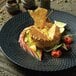 A black Luzerne Urban by Oneida porcelain coupe plate with food on it on a table.