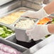 A person in gloves holding a Vollrath stainless steel steam table pan of food.