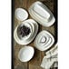 A stack of white plates and bowls with a white sauce dish on a wood surface.