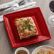 A Tuxton Concentrix cayenne square plate with food on it on a table with silverware and a white napkin.