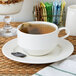 A Oneida warm white porcelain coupe saucer with a cup of tea on it.