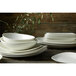 A stack of Oneida Stage warm white porcelain bowls on a wooden table.