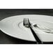 A close-up of a fork and knife on a Oneida Manhattan warm white porcelain plate.