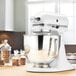 A white KitchenAid Artisan Series countertop mixer on a wooden counter.