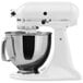 A white KitchenAid Artisan countertop mixer with a bowl on top.