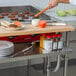 A chef preparing food on a Regency stainless steel plate shelf on a long kitchen counter.