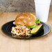 A Fineline black plastic plate with a sandwich and a cup of coffee on a table.