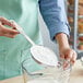 A person using a Thunder Group stainless steel measuring scoop to pour flour into a bowl.