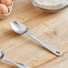 A stainless steel measuring scoop on a wooden table with flour and eggs.