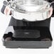 A person holding a silver pot over a black surface with a black Vollrath non-slip silicone chafer mat inside.