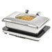 A Vollrath stainless steel chafing dish with a glass lid on a counter with food inside.