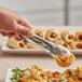 A person holding American Metalcraft stainless steel serving tongs over food.