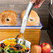 A hand holding an American Metalcraft stainless steel salad fork over a plate of salad.