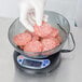 A person in gloves weighing meat on a Globe portion control scale.