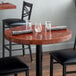 A Lancaster Table & Seating round wooden table with glasses and a napkin on it.