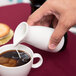 A person pouring milk into a cup of coffee using an Arcoroc creamer.