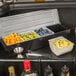 A black Choice condiment holder insert on a counter with bowls of limes, orange slices, and lemon slices.