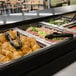 A black Cambro buffet with a sneeze guard filled with food on a table.