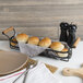 A Tablecraft black powder coated condiment caddy on a table with a bread basket and knife.