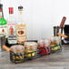 A black metal Tablecraft condiment caddy holding jars and bottles of lemons, cherries, and olives.